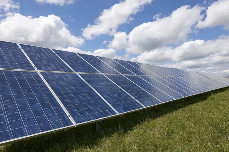Rows of solar panels installed across a green grass field under a blue sky with white clouds