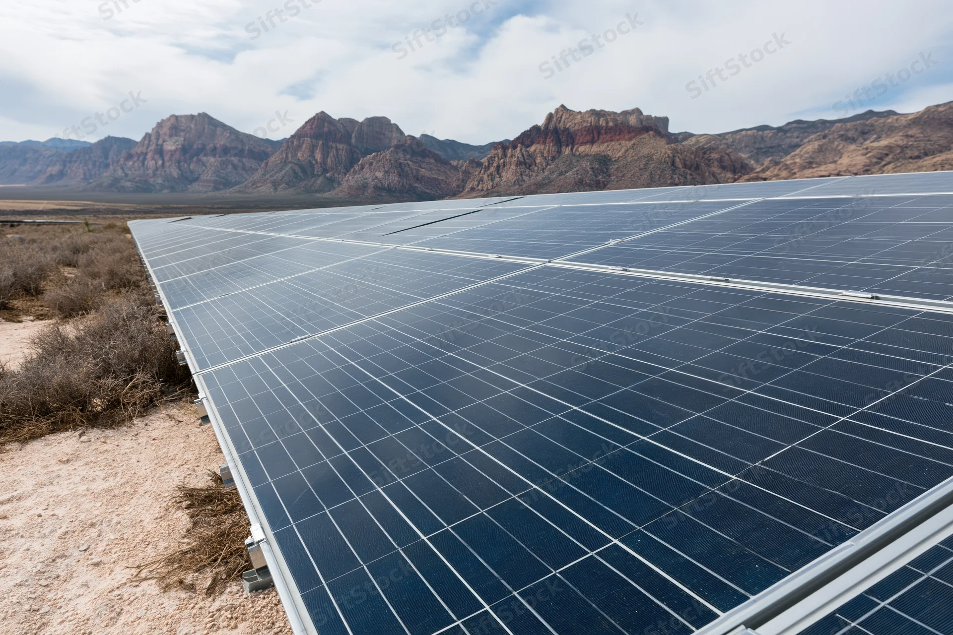 Rows of solar panels arranged in a flat desert landscape with rocky mountains in the background