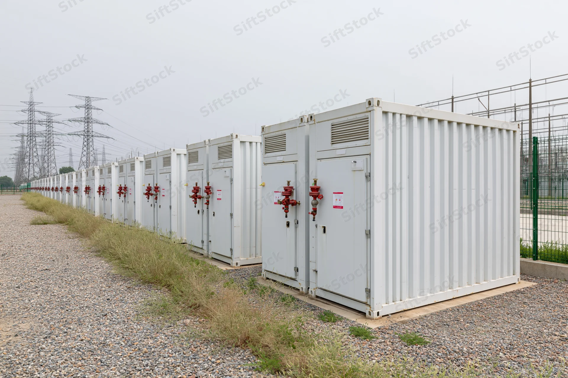 Rows of white industrial battery energy storage containers arranged outdoors near power transmission lines