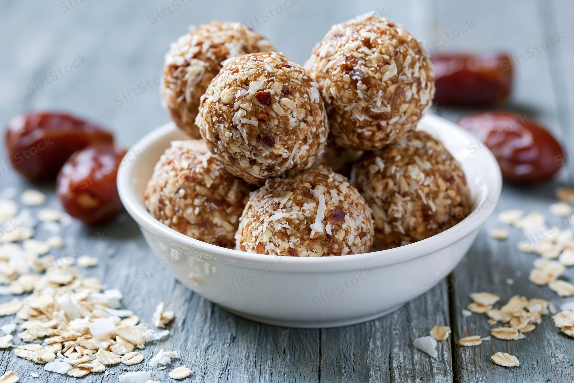 No-bake oat and date energy balls piled in a shallow white bowl on a rustic wooden table
