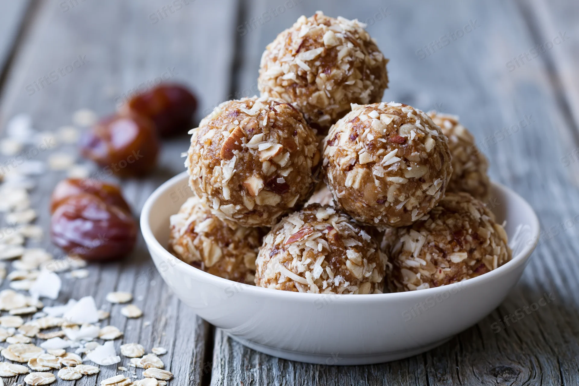 No-bake oat and date energy balls piled in a white bowl on a wooden table