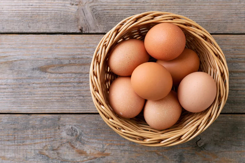 Brown chicken eggs in a round wicker basket on a wooden table