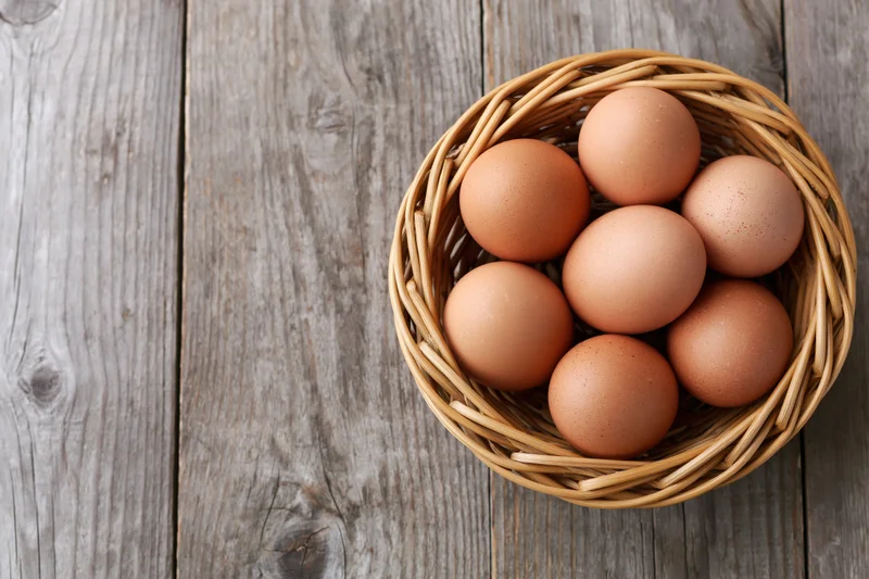 Brown chicken eggs arranged in a round wicker basket on a rustic wooden table