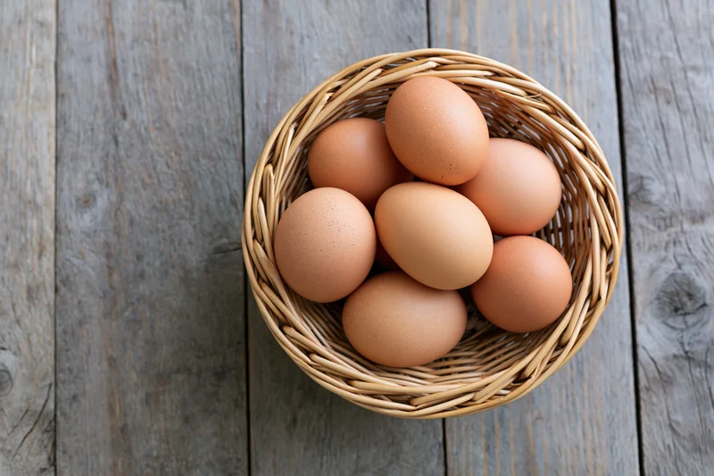 Brown chicken eggs arranged in a round wicker basket on a rustic wooden table