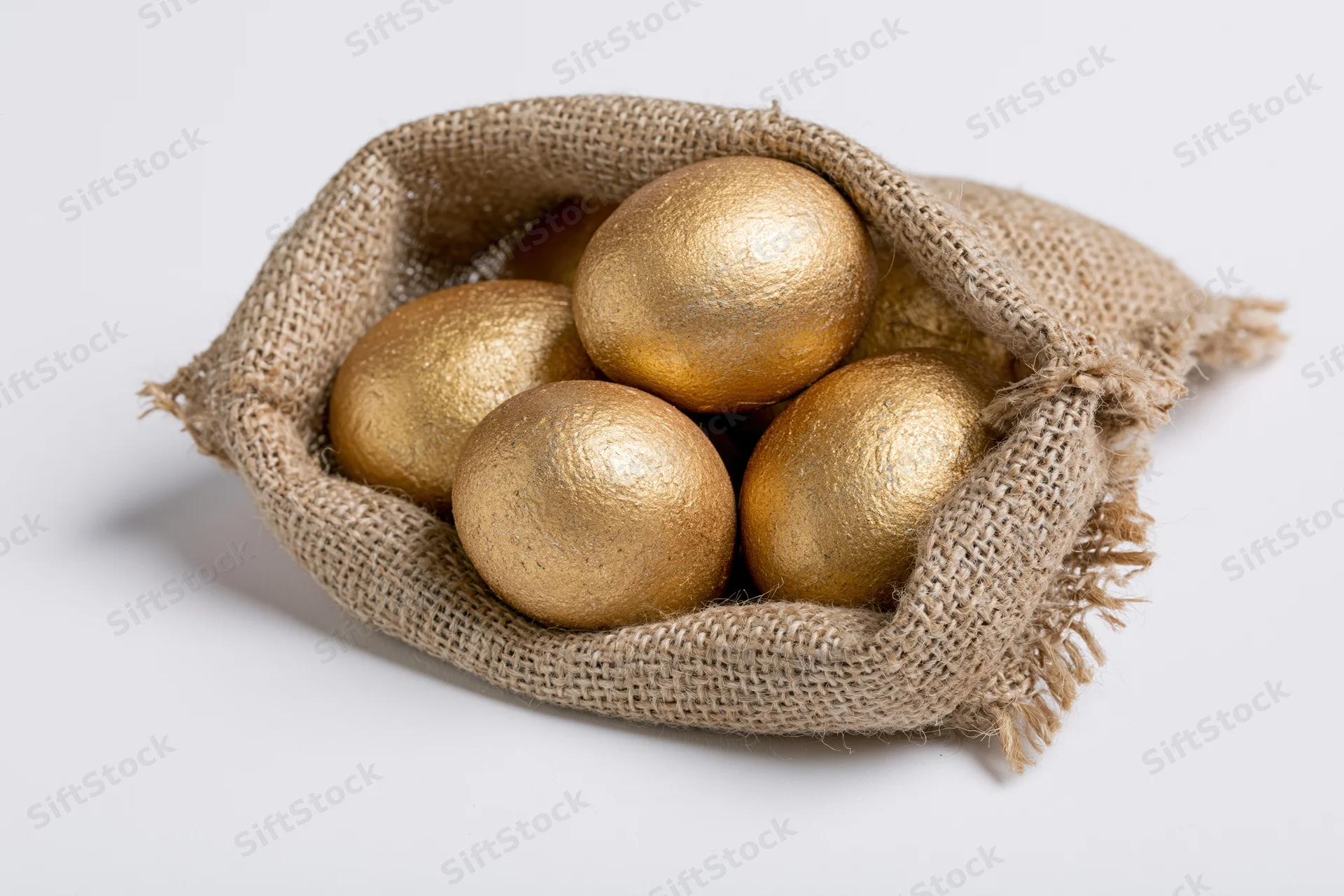 Gold-painted eggs nestled in an open burlap sack on a white background