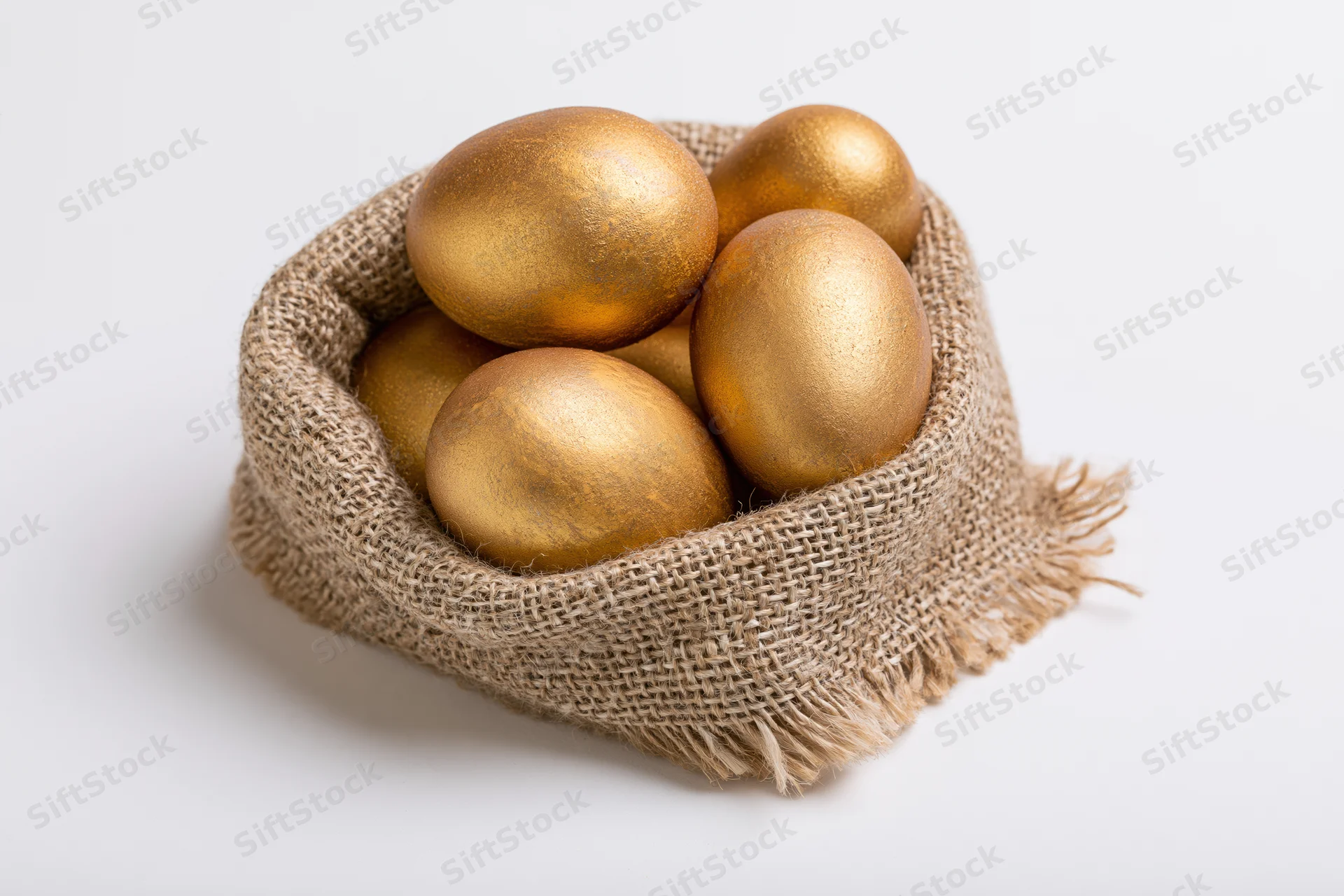 Gold-painted eggs nestled in a small open burlap sack on a white surface