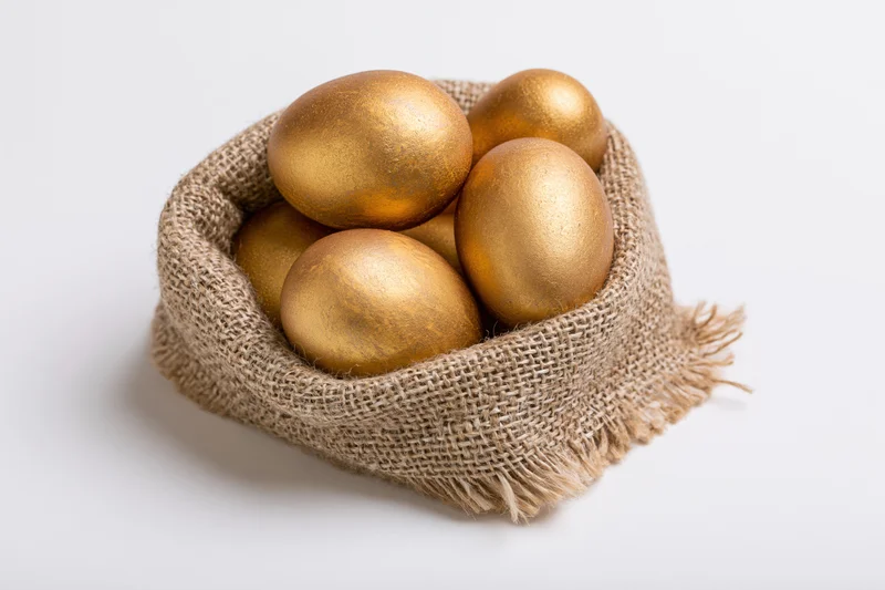 Gold-painted eggs nestled in a small open burlap sack on a white surface