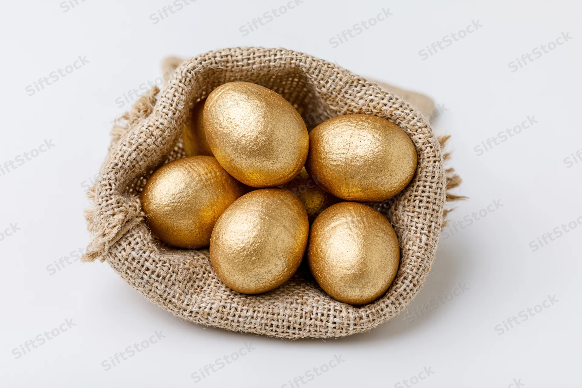 Gold-painted eggs nestled in an open burlap sack on a white surface