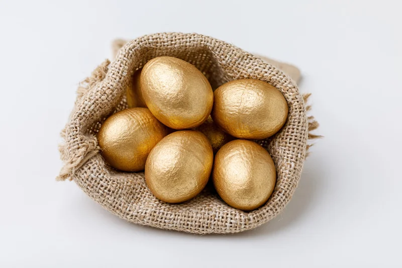 Gold-painted eggs nestled in an open burlap sack on a white surface