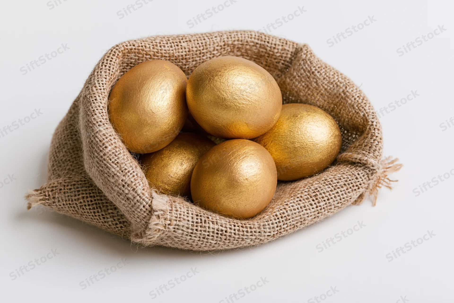 Gold-painted eggs nestled in an open burlap sack on a white surface
