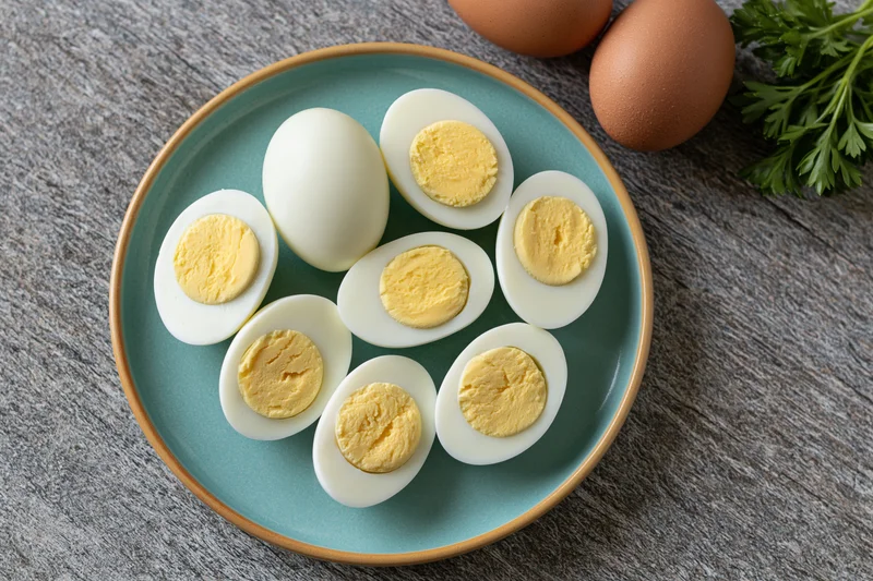 Halved hard-boiled eggs arranged on a blue ceramic plate with whole eggs and parsley on a wooden surface