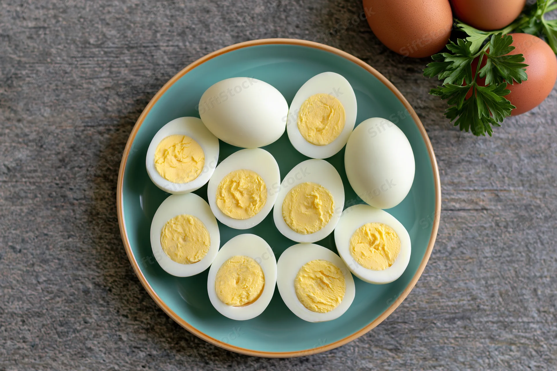 Halved hard-boiled eggs arranged on a pale blue ceramic plate with parsley garnish on a gray wooden surface