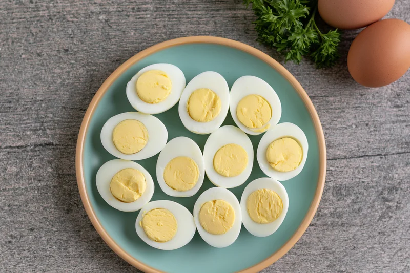 Halved hard-boiled eggs arranged in a circle on a pale blue ceramic plate with whole eggs and parsley nearby on a gray wooden surface
