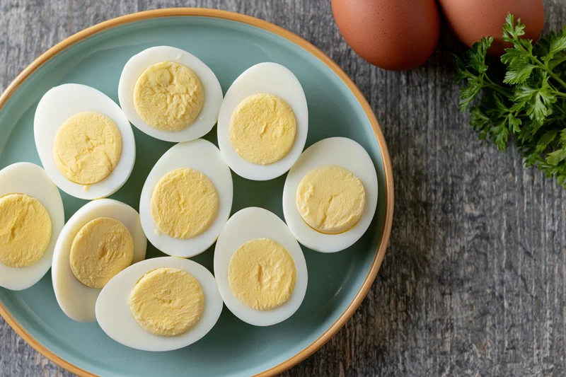 Halved hard-boiled eggs arranged on a pale blue ceramic plate with parsley and whole eggs on a wooden surface