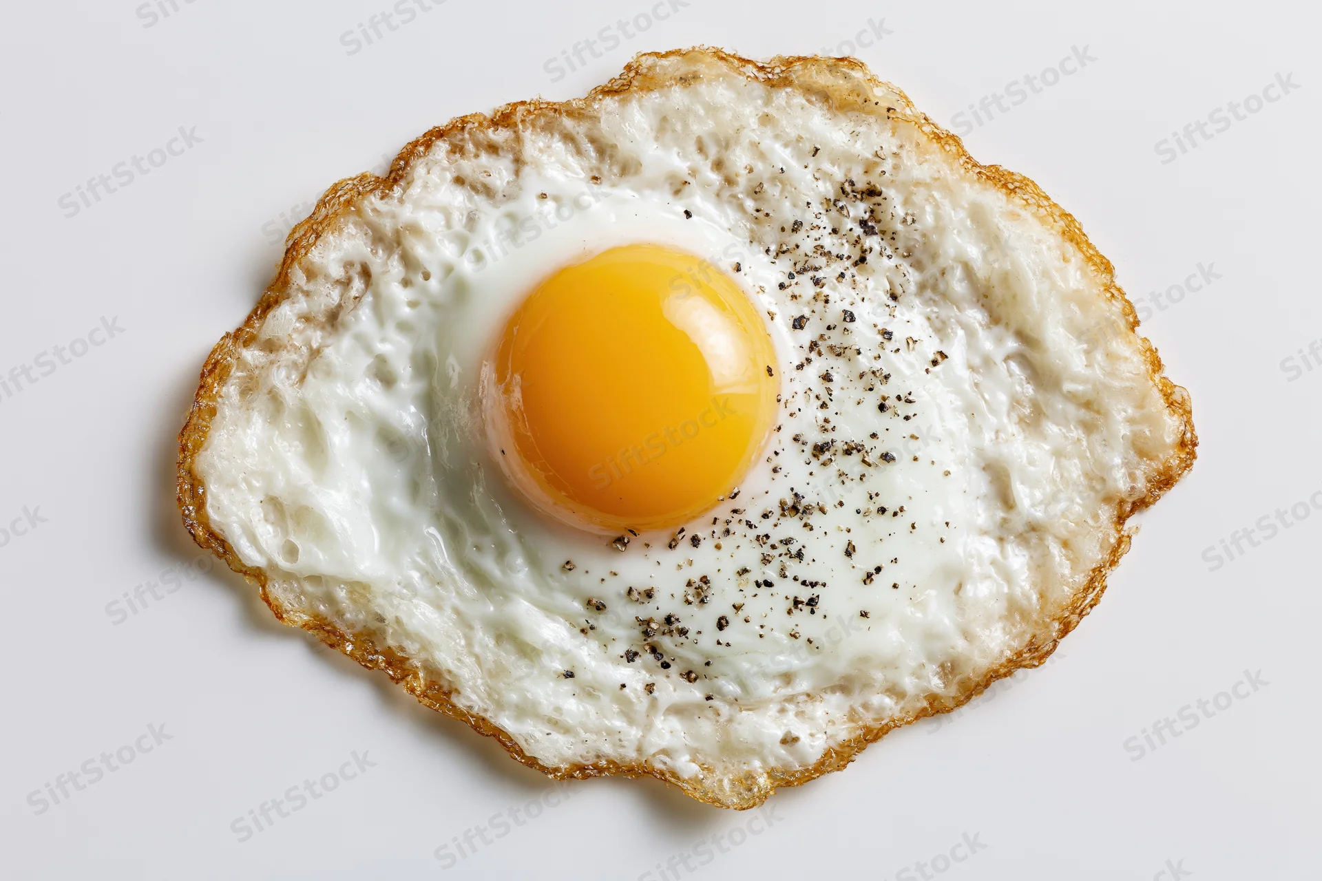 Single fried egg with runny yolk and pepper seasoning centered on white background
