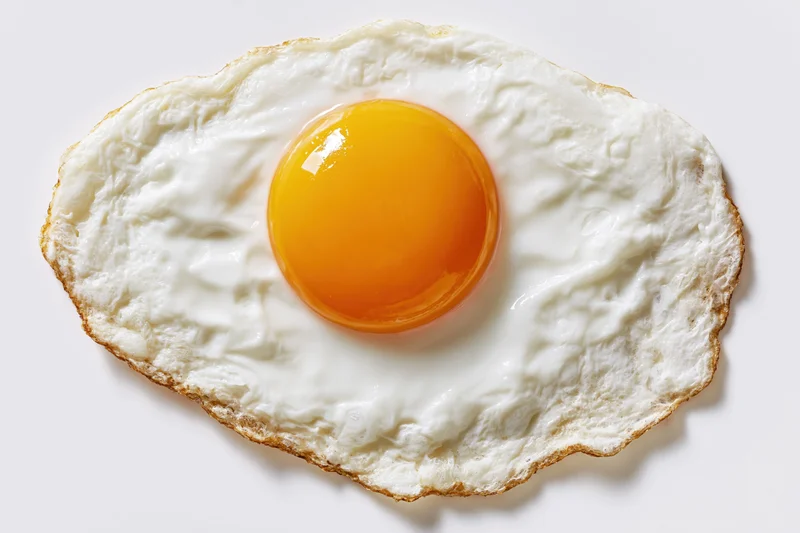 Single fried egg sunny side up viewed from directly overhead on white surface