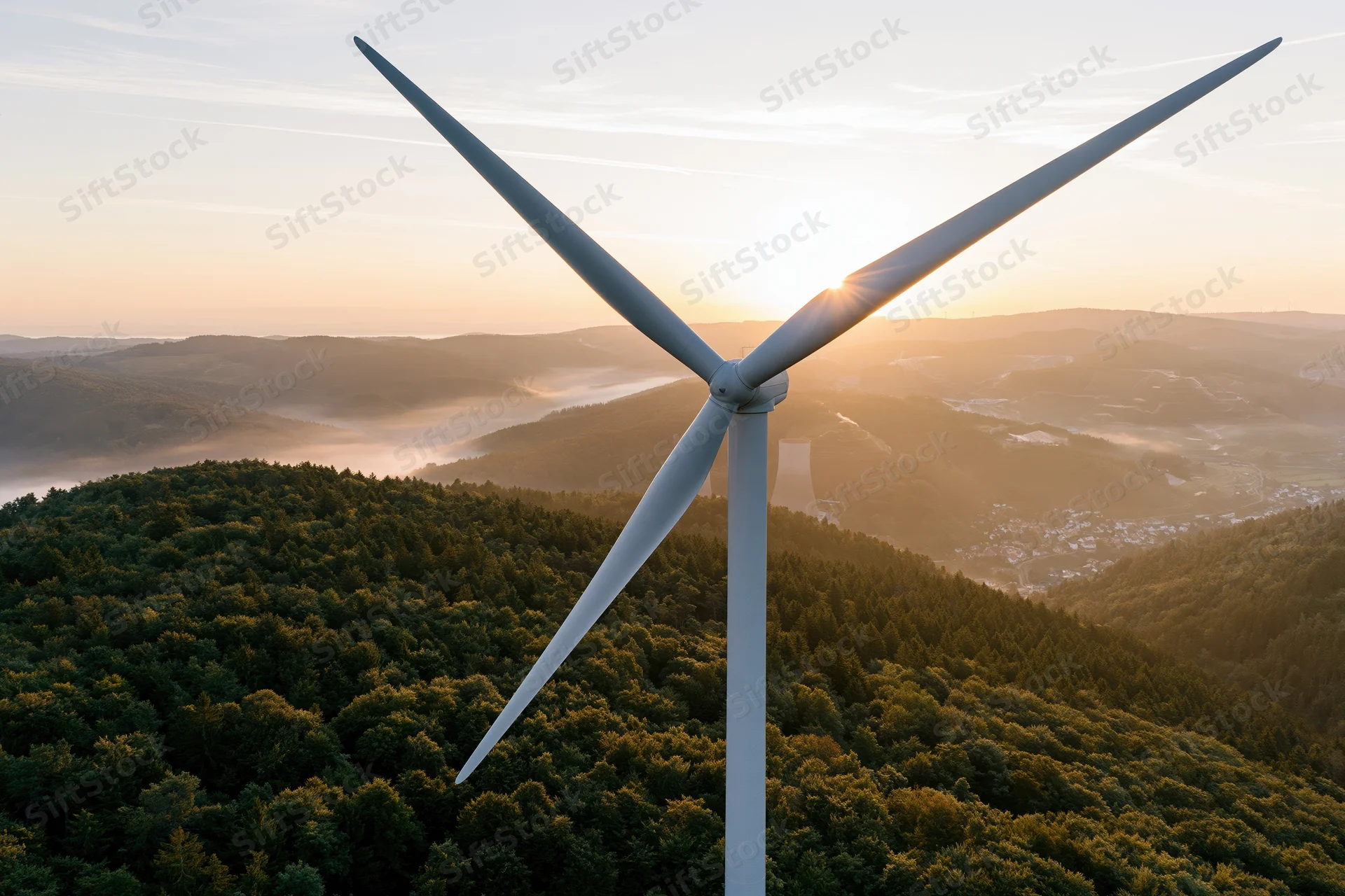 Single wind turbine rising above dense rolling forest at sunrise
