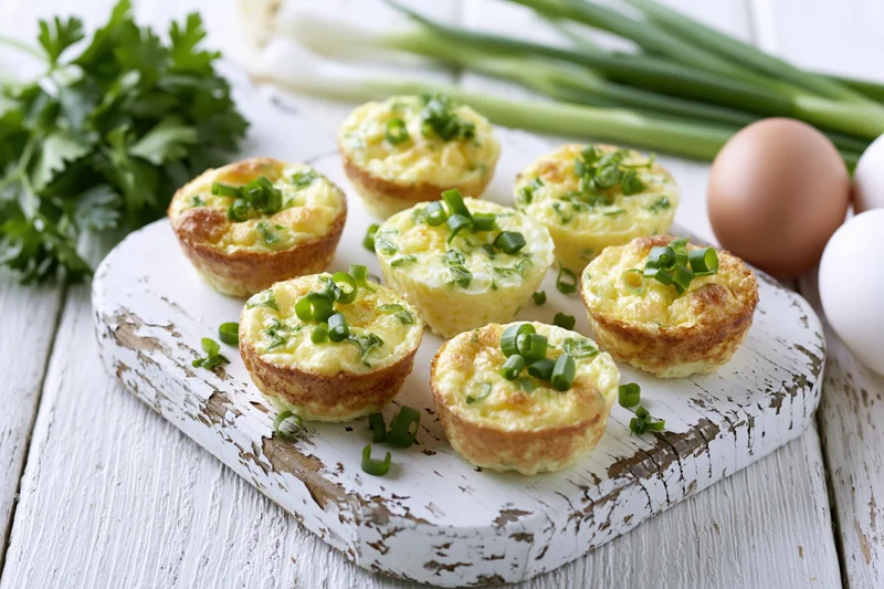 Baked egg muffin cups topped with chopped green onion on a rustic white cutting board