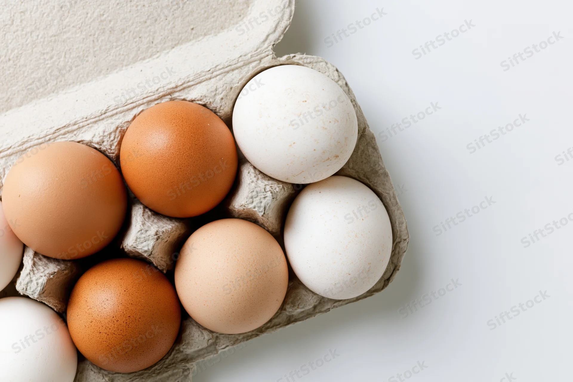 Brown and white chicken eggs arranged in an open cardboard carton on a white surface