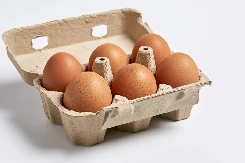 Six brown chicken eggs arranged in an open cardboard carton on a white surface