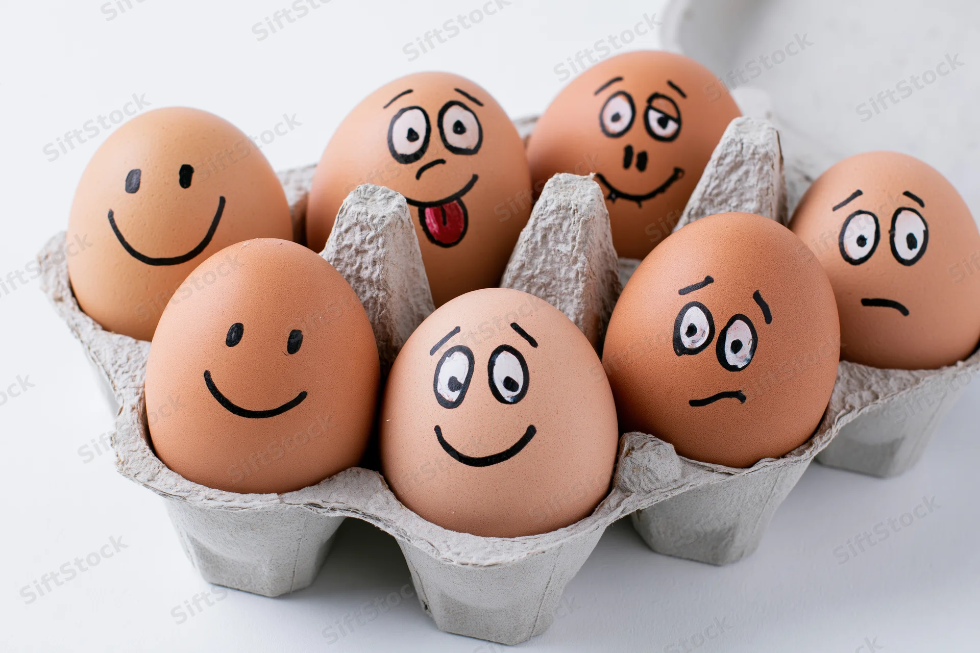 Six brown eggs with hand-drawn cartoon faces in a gray cardboard egg carton on a white background