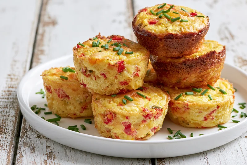 Egg muffin bites stacked on a white plate on a rustic wooden table