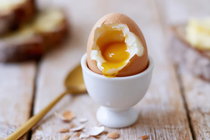 Soft-boiled egg cracked open with runny yolk in a white ceramic eggcup on a wooden table