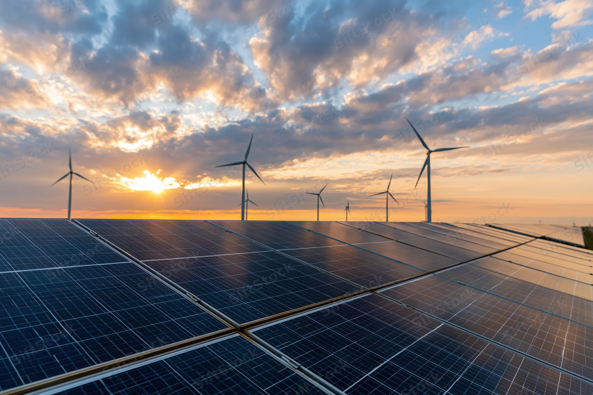 Solar panels in a grid formation with wind turbines in the background at sunset
