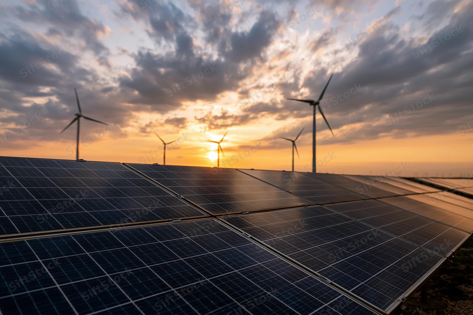 Solar panels in a field with wind turbines at sunset