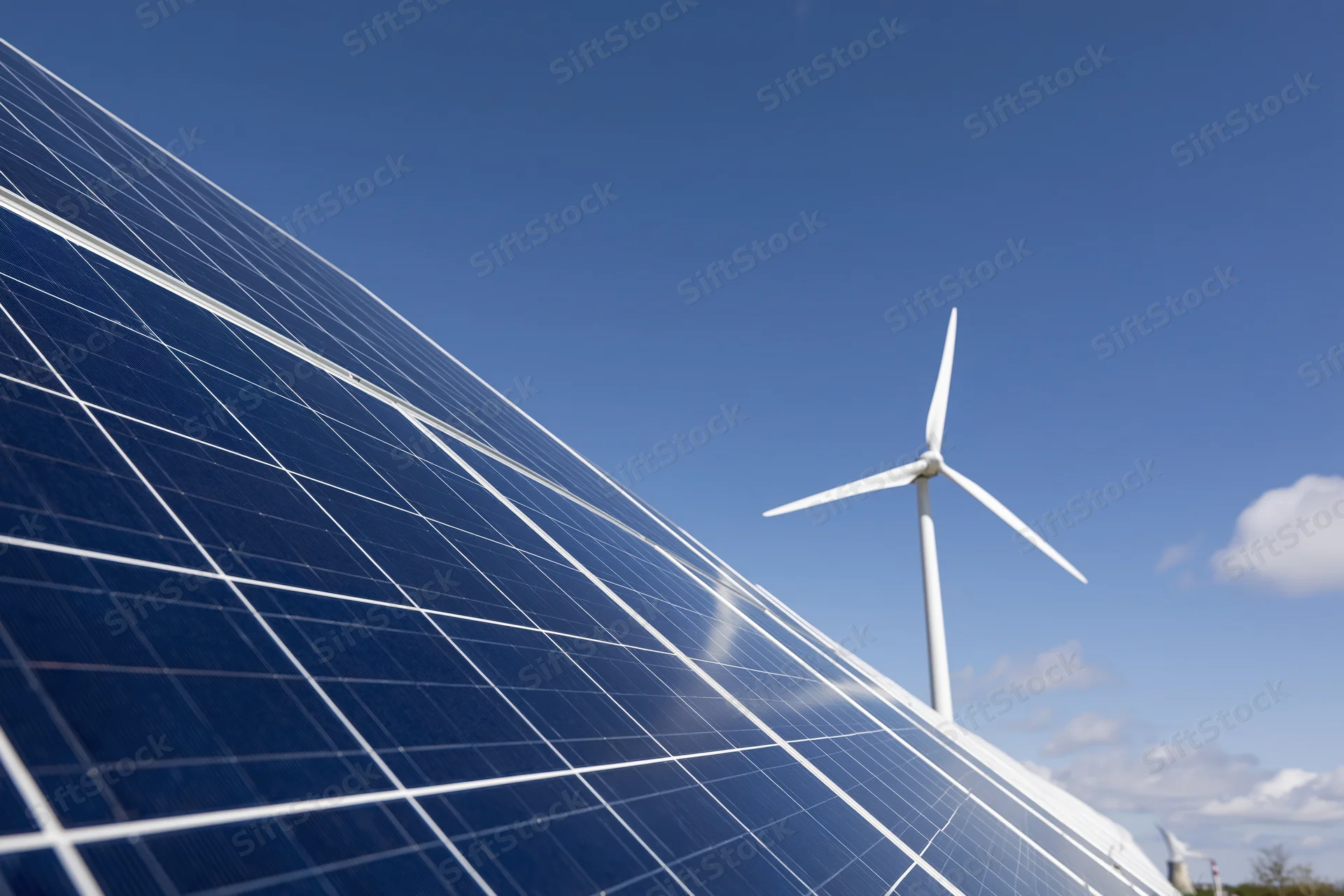 Solar panel array filling foreground with wind turbine in background under clear blue sky