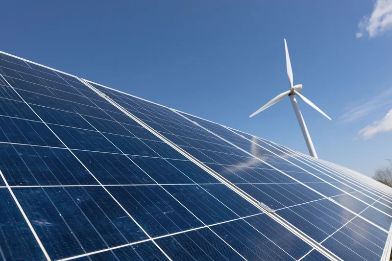 Solar panel array filling foreground with wind turbine in background under clear blue sky