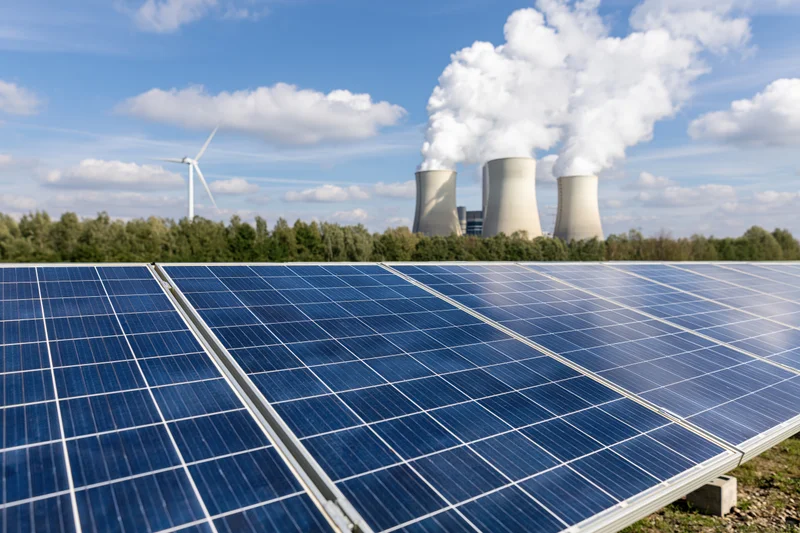 Solar panels in a field with a coal power plant and wind turbine in the background