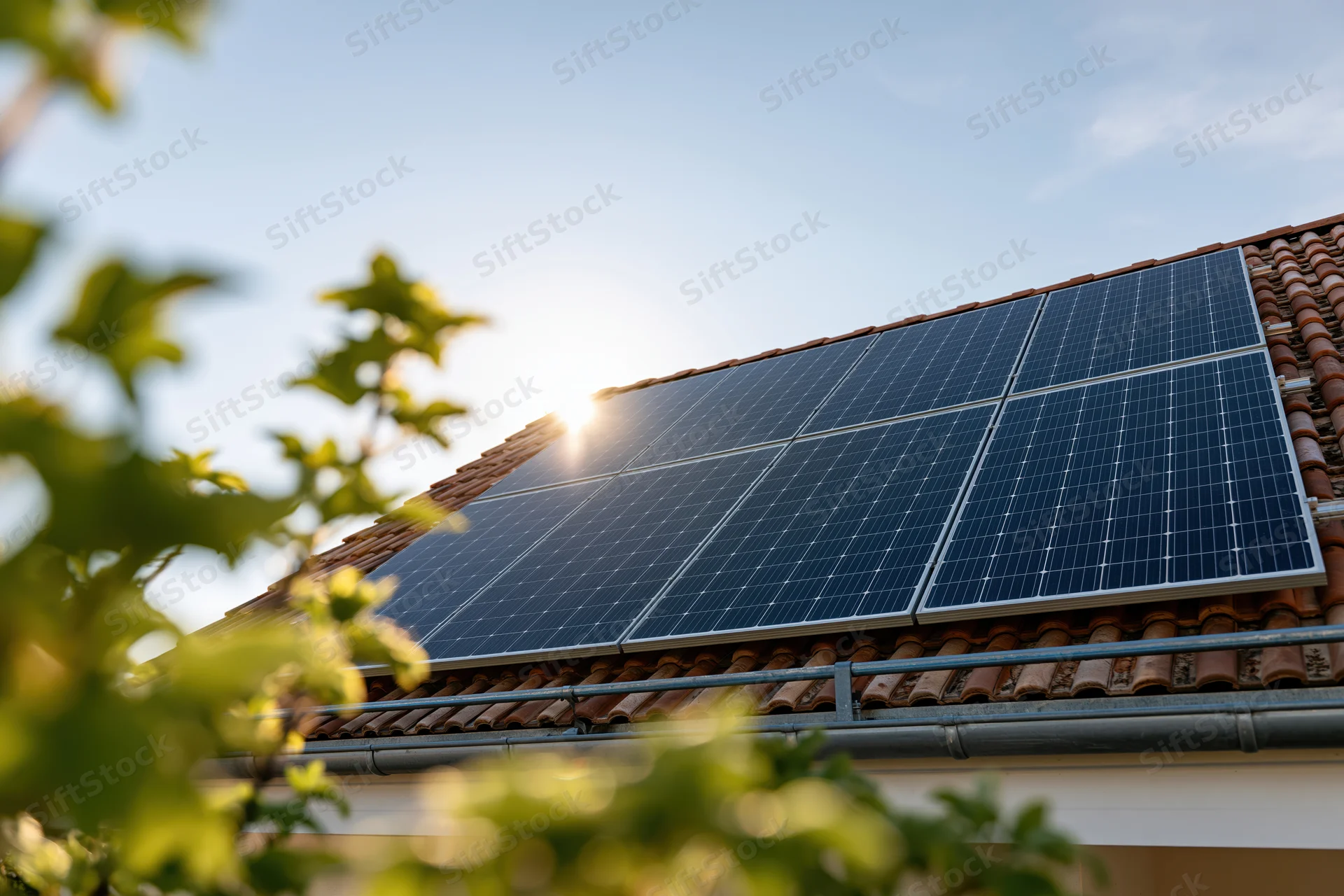 Solar panels mounted on a residential tiled rooftop with sunlight and foliage in foreground