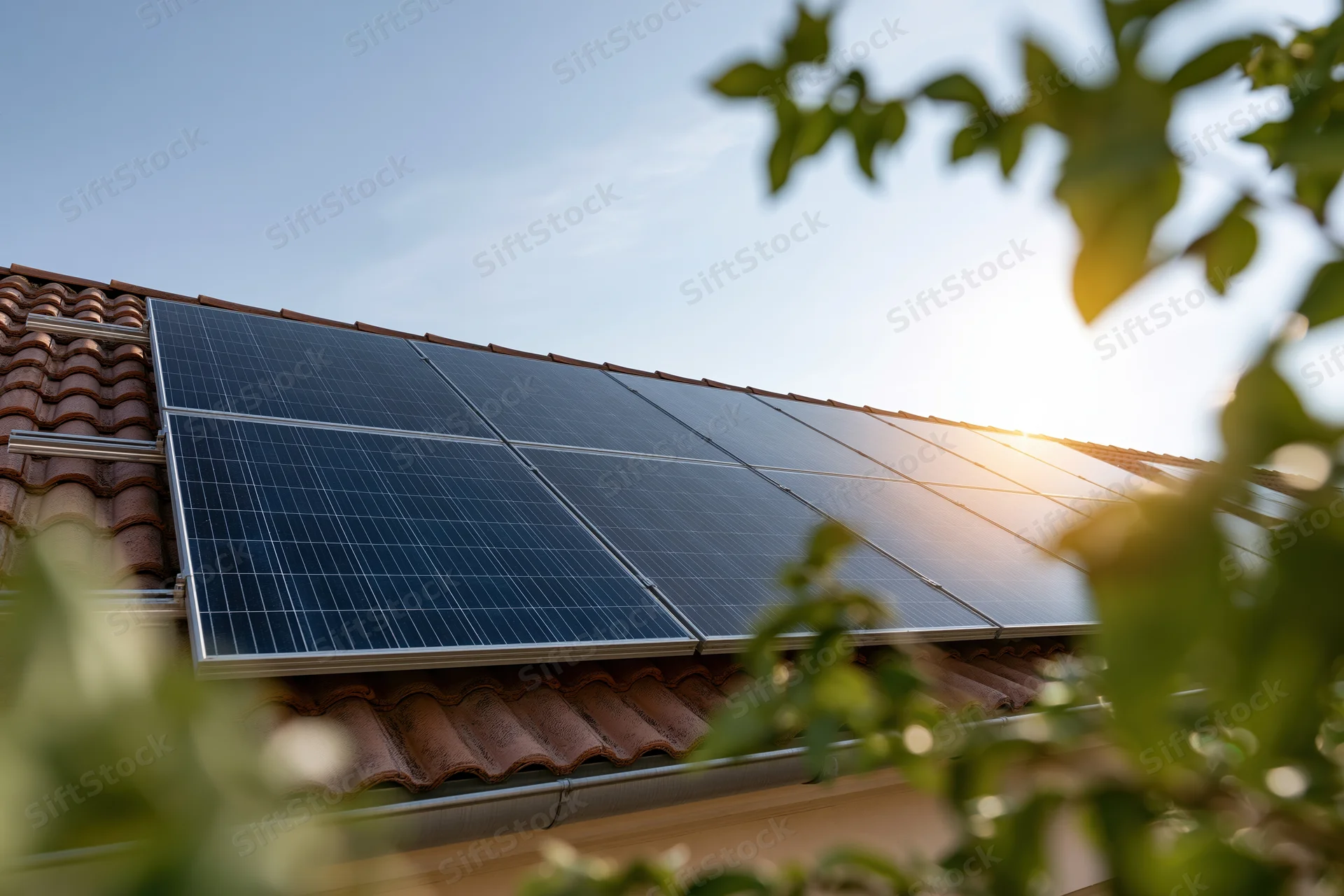 Solar panels mounted on a residential tiled rooftop with sunlight and foliage in view