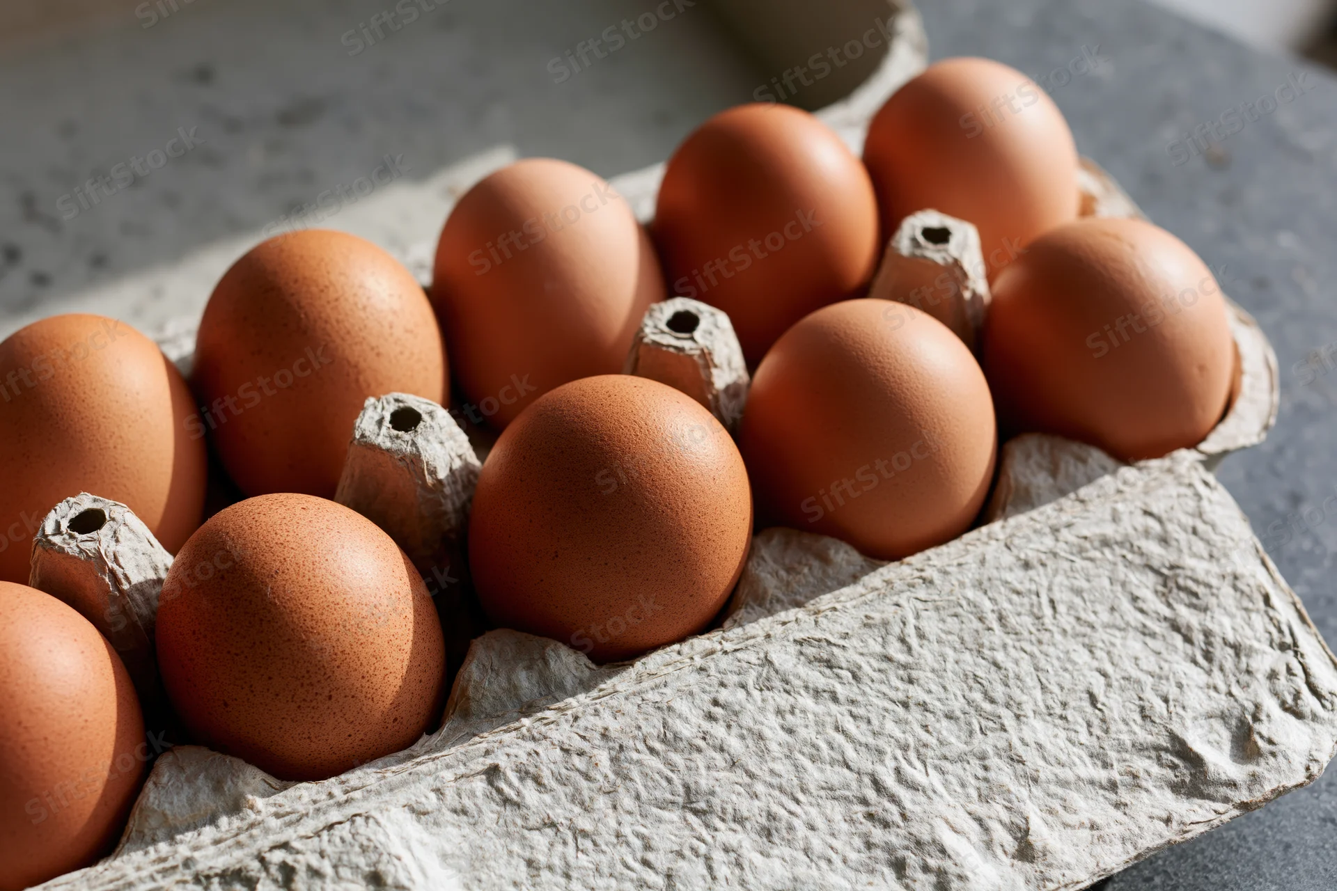Ten brown chicken eggs arranged in an open cardboard egg carton on a textured surface