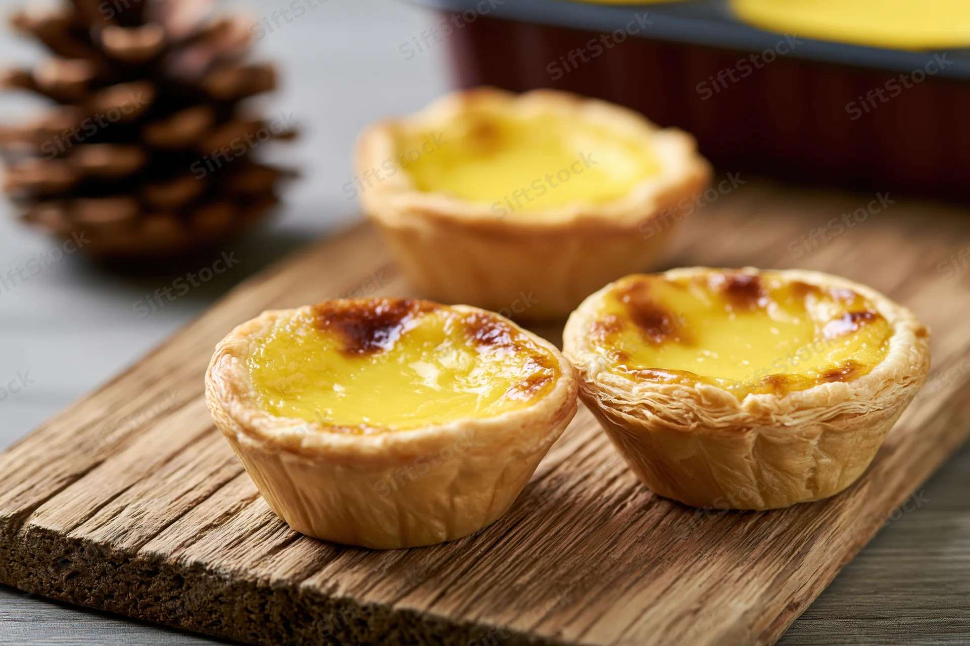 Three hong kong-style egg tarts with flaky puff pastry shells arranged on a wooden board