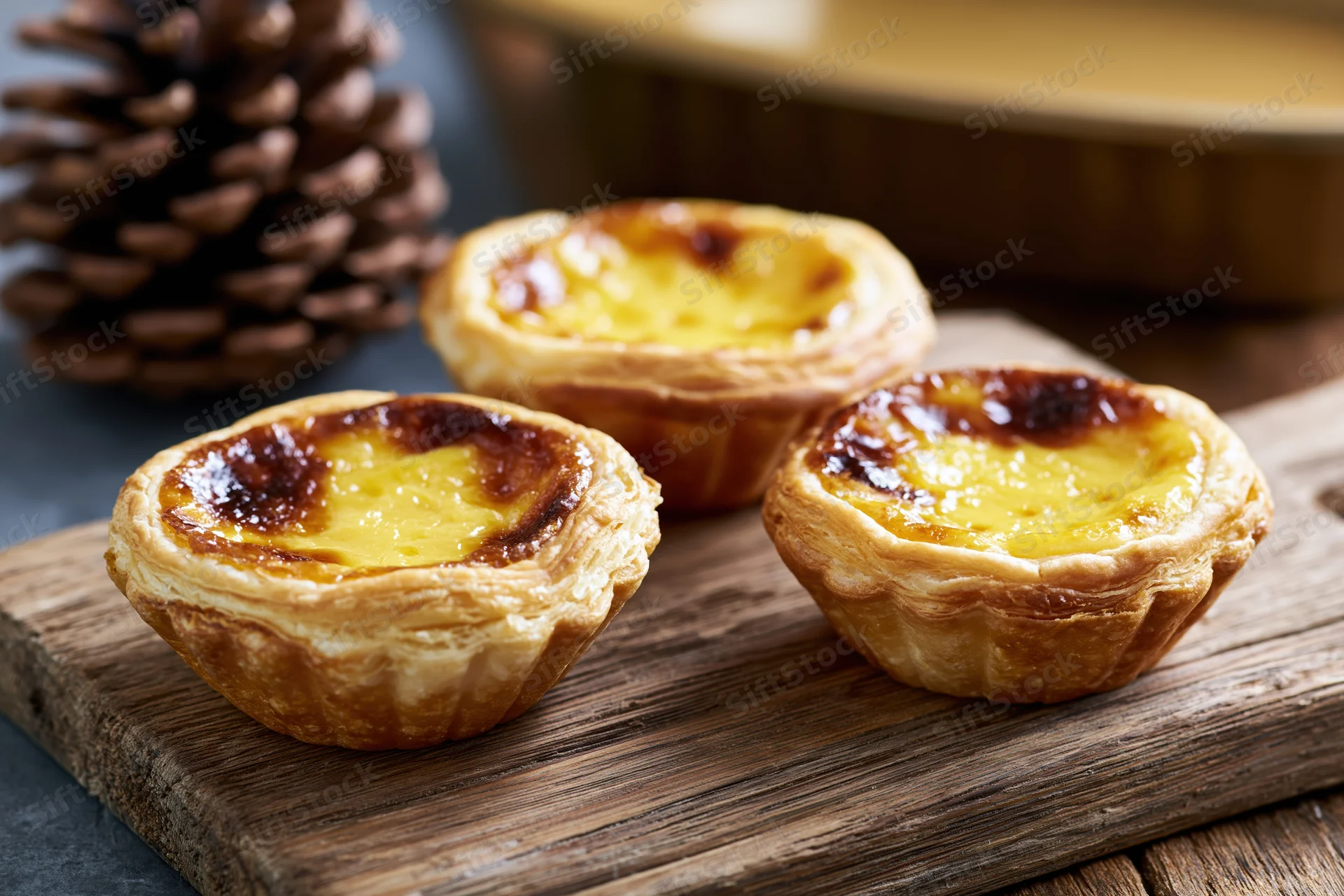 Three hong kong style egg tarts with flaky puff pastry shells arranged on a wooden board