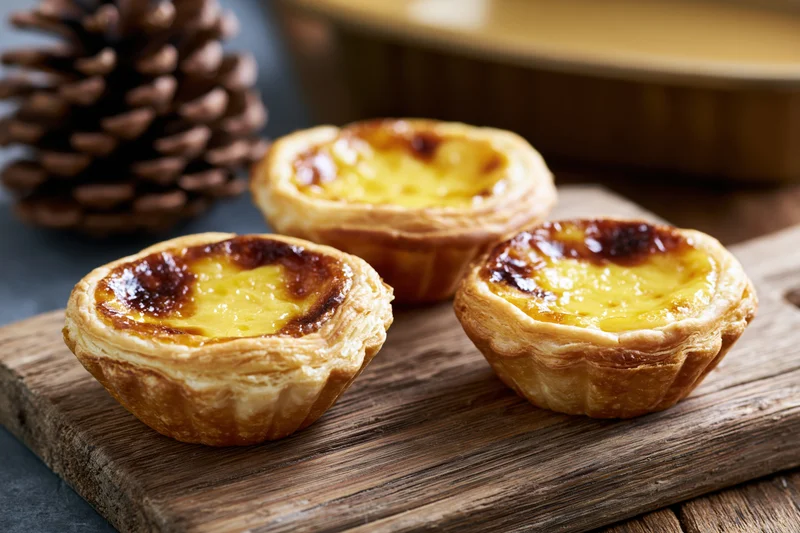 Three hong kong style egg tarts with flaky puff pastry shells arranged on a wooden board