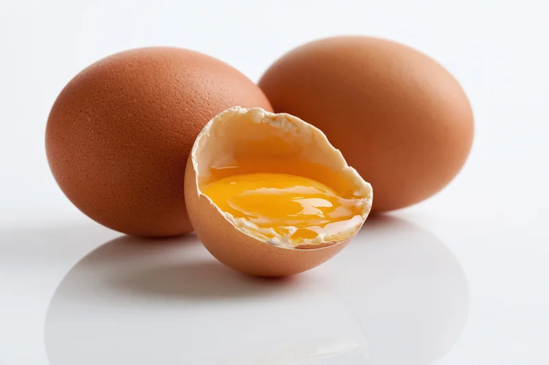 Three brown chicken eggs on white surface one cracked open showing yolk