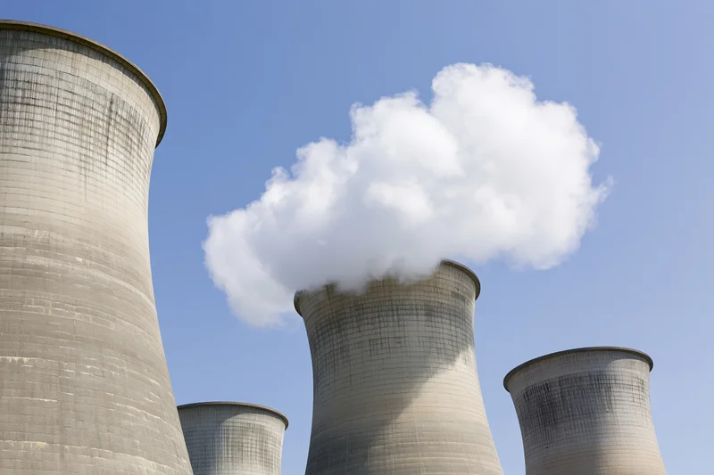 Concrete cooling towers emitting steam against a clear blue sky