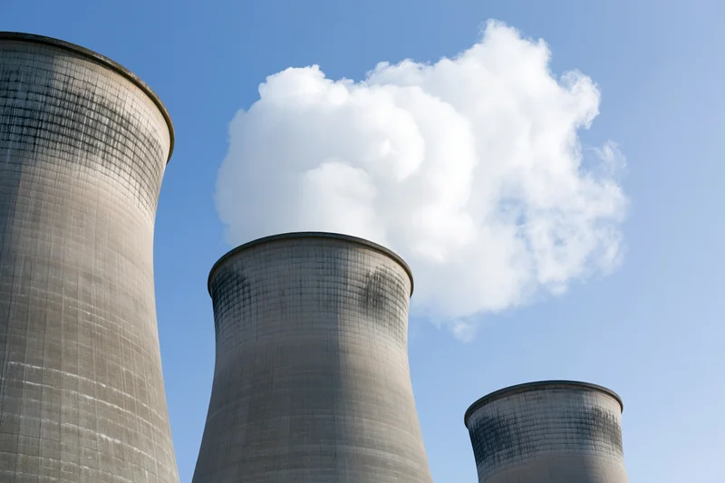 Three concrete cooling towers emitting steam against a clear blue sky