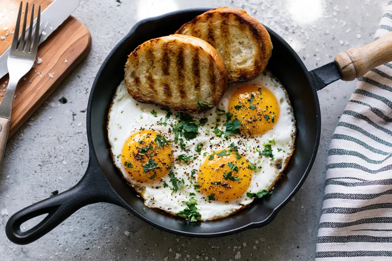 Three fried eggs with golden yolks and grilled toast in a cast iron skillet on a kitchen countertop