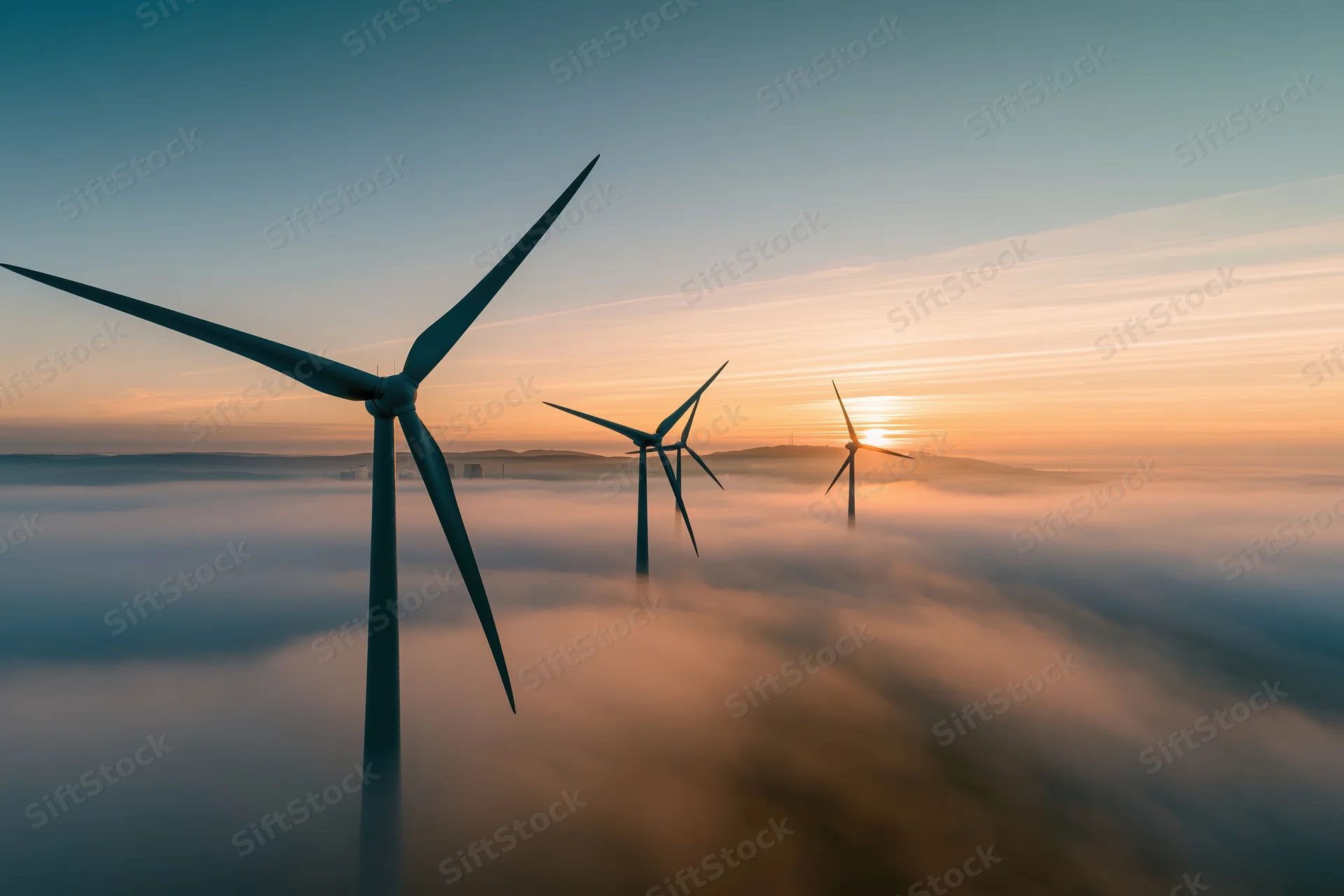 Wind turbines rising above a fog bank at sunrise
