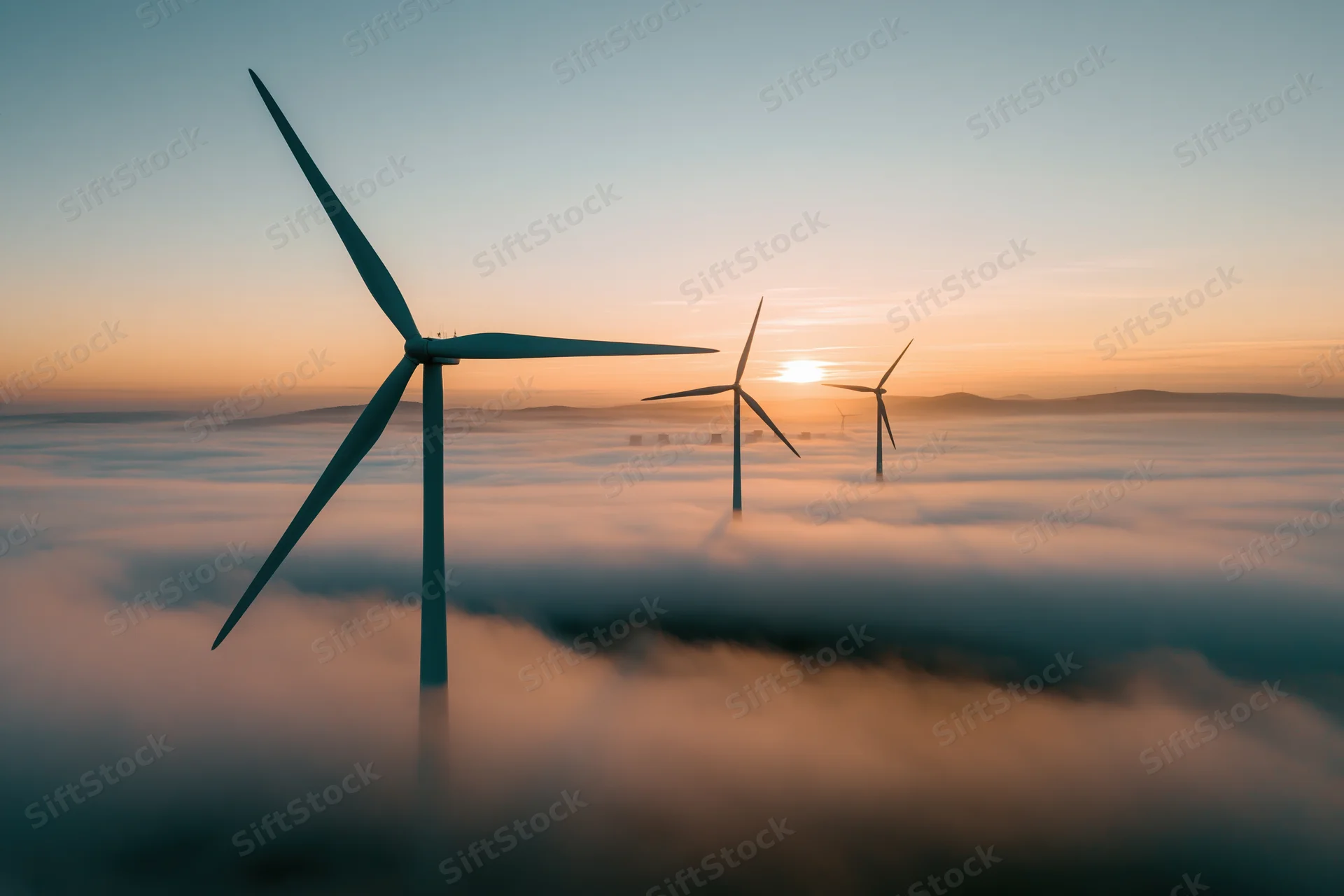 Wind turbines rising above a fog bank at sunrise