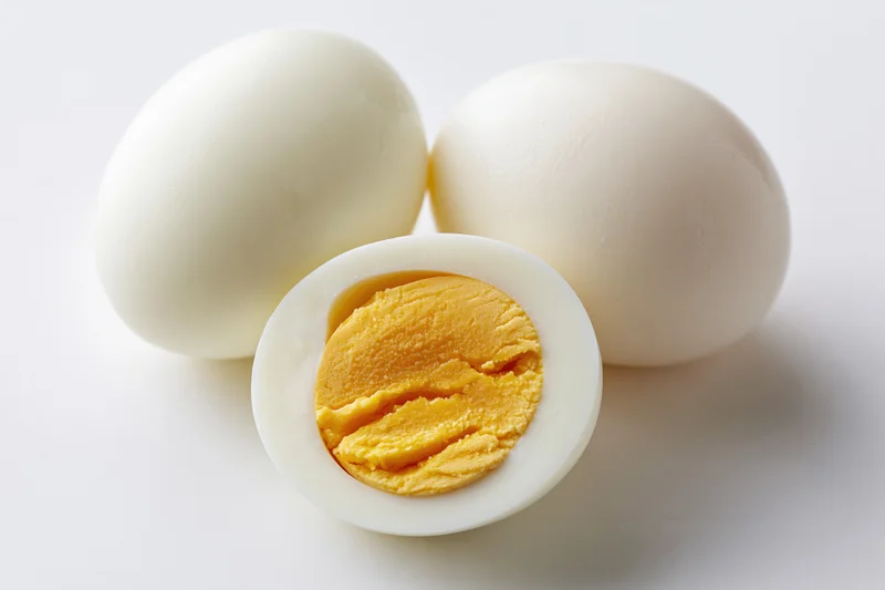 Three peeled hard-boiled eggs on white surface with one halved to show yolk