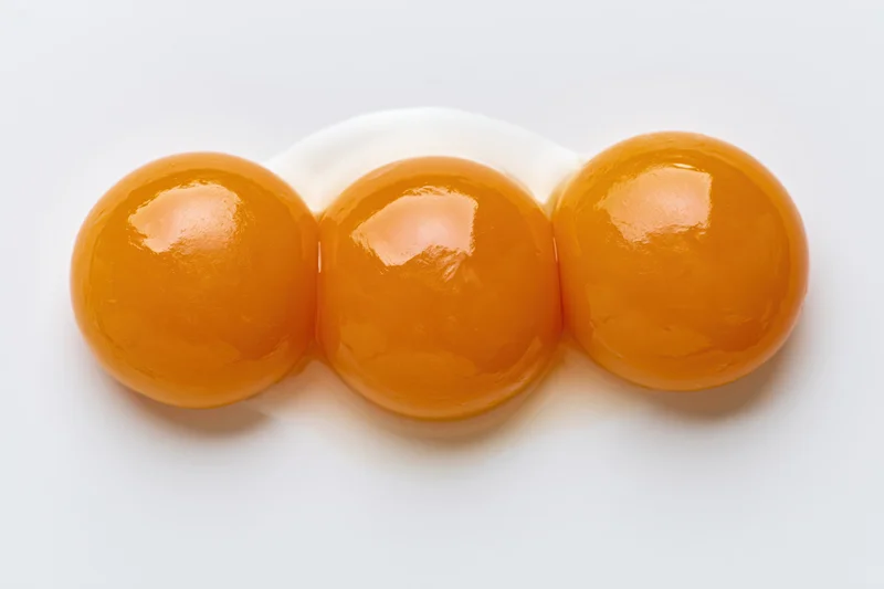 Three raw egg yolks arranged in a tight cluster on a plain white surface