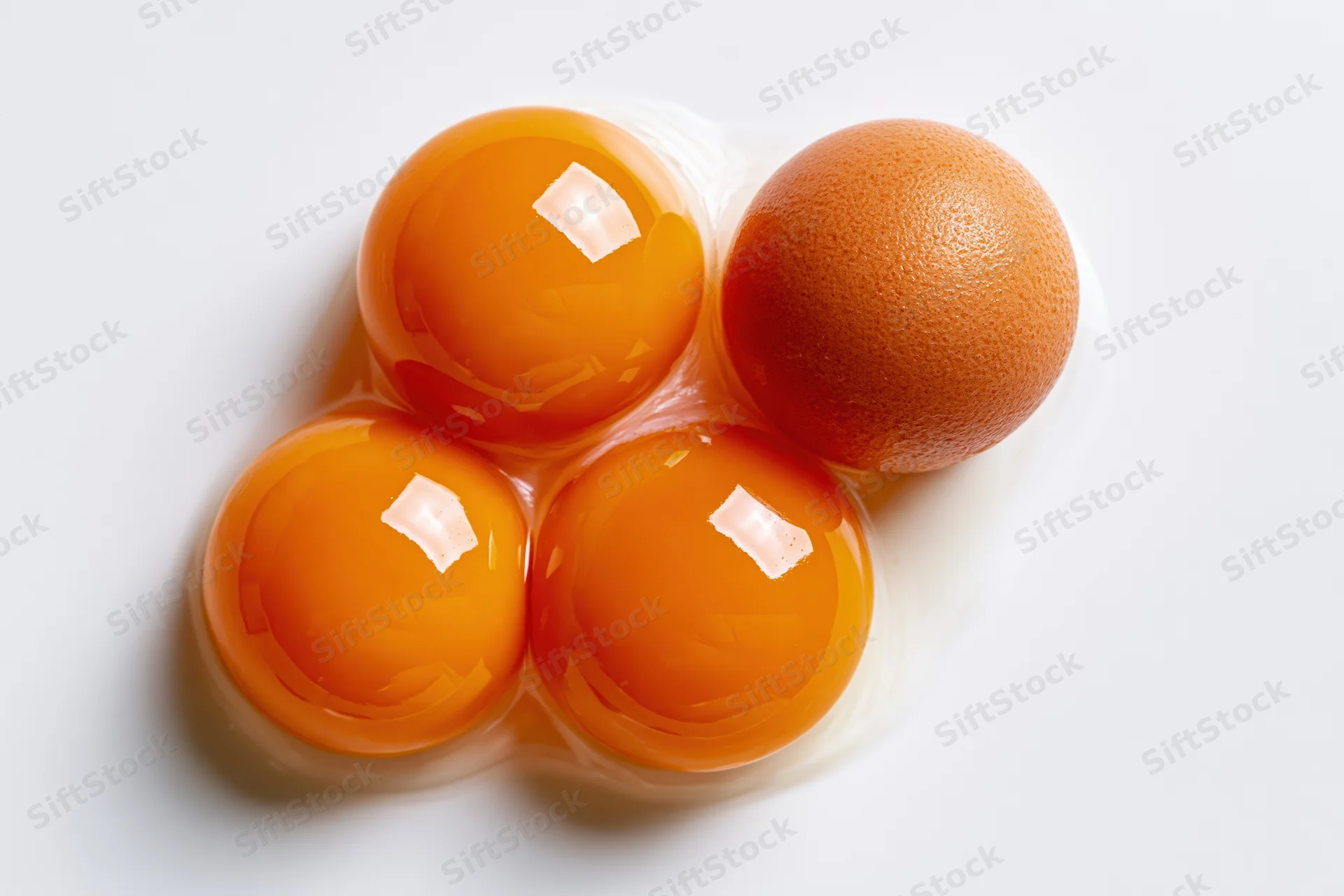 Three raw egg yolks clustered with one whole egg on white surface