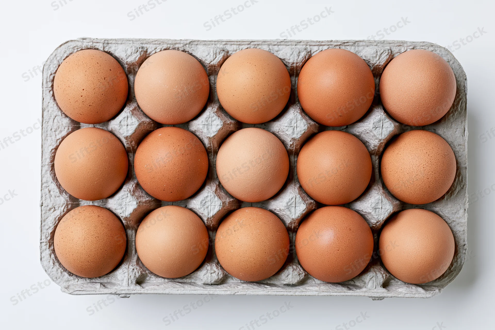 Twelve brown chicken eggs arranged in a gray recycled cardboard carton on white background