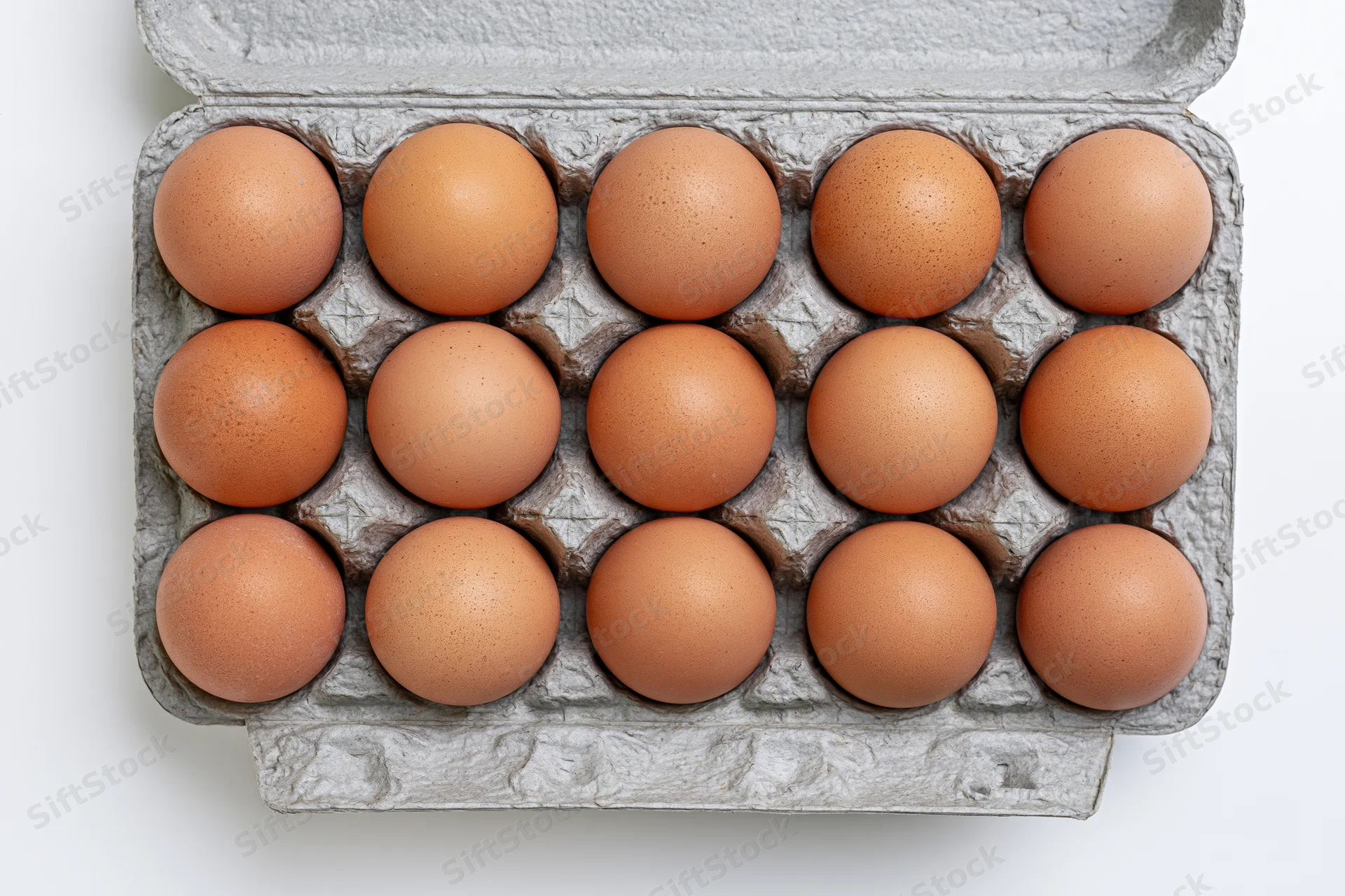 Twelve brown chicken eggs arranged in a gray recycled cardboard carton on white background