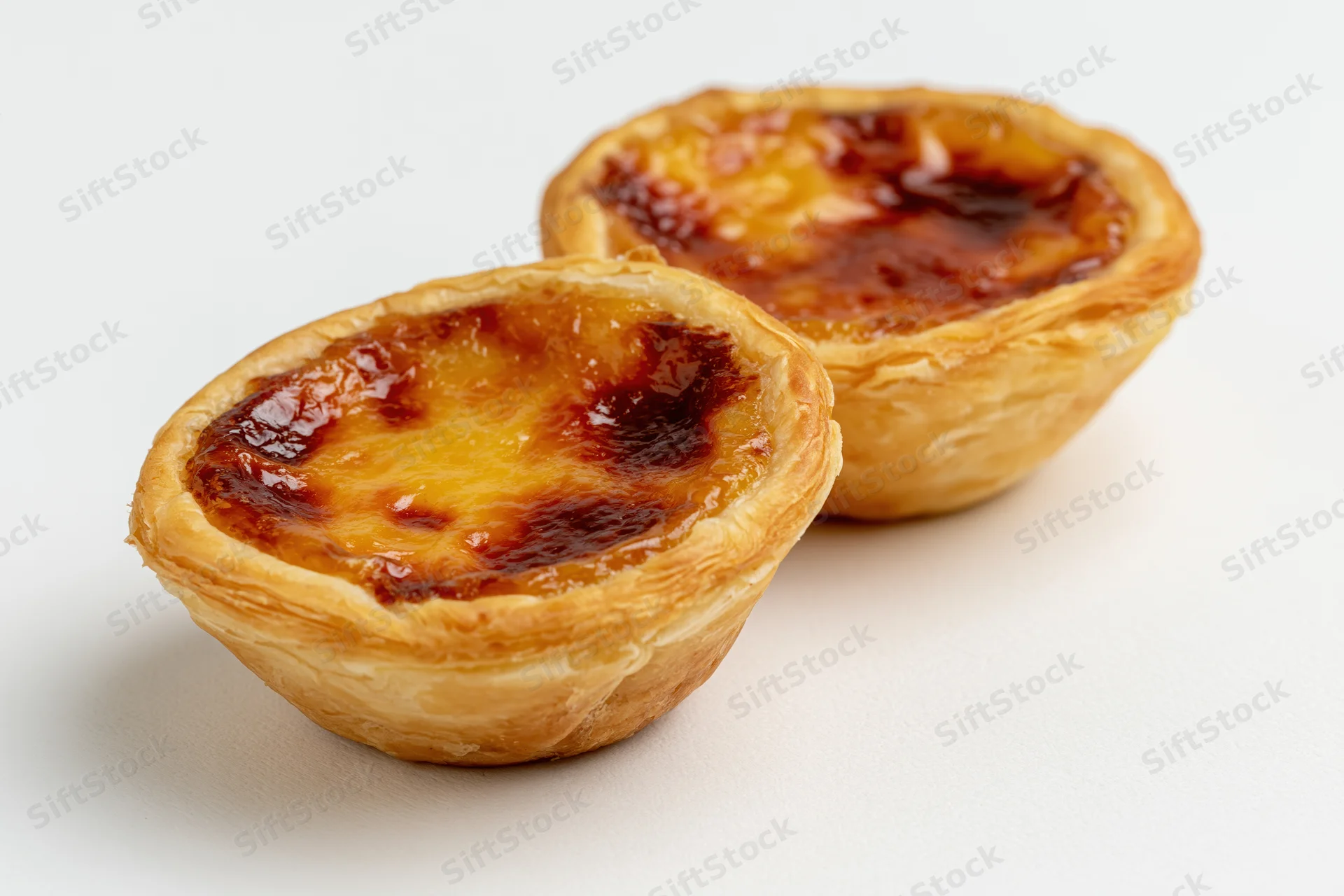 Two portuguese pastel de nata egg tarts placed close together on white surface